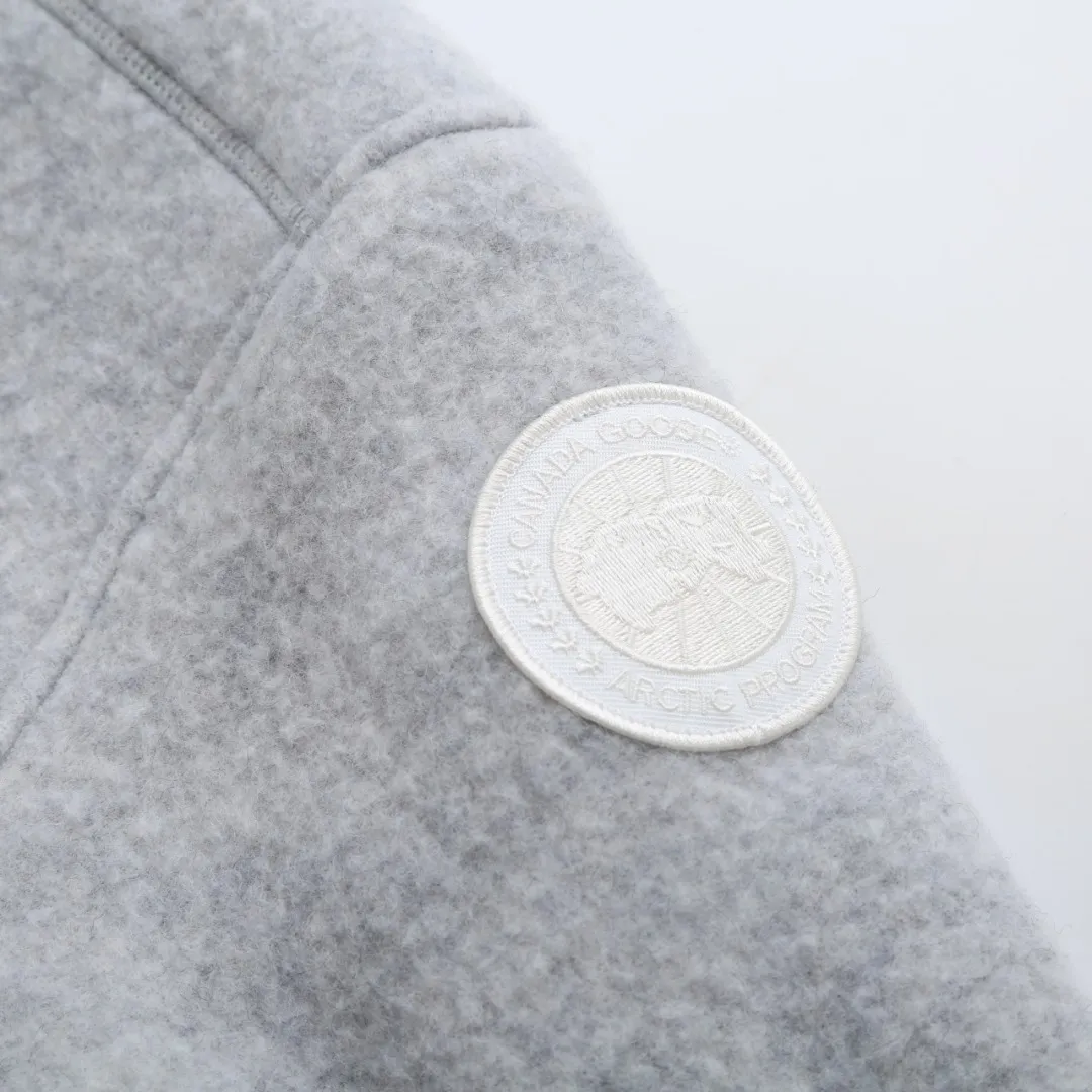 P760 Canada Goose Fleece Badge Button Jacket Fabric selection: Wool blend fabric: The main fabric of this jacket is light gray wool blend fabric to improve the fabric's wear resistance, wrinkle resistance and warmth. Wool provides good warmth and a natural feel, while blended fibers enhance the fabric's practicality and durability.  RIBBED KNIT: The collar, cuffs and hem are ribbed knitted for added stretch and fit.  Production process: The cutting process needs to ensure that the texture and color of the fabric are evenly distributed, especially for this light gray tone, to avoid color differences. The stretchability of wool-blend fabrics needs to be taken into consideration when cutting pieces to ensure dimensional stability of the finished garment.      • Use a sewing needle and thread suitable for wool-blend fabrics to avoid damage to the fabric during sewing. The sewing stitches are even and firm to prevent thread stripping.      • The temperature needs to be controlled during ironing to avoid high temperature damage to the fabric while keeping the fabric smooth and crisp.  Main body splicing: • The front and back body parts, sleeves and other main parts are spliced ​​with flat seams to ensure a smooth silhouette. •Align the fabric texture at the splicing points to keep the appearance neat.     Details such as pockets and cuffs are designed with inset pockets to increase practicality and aesthetics.     The splicing areas are reinforced to improve durability.  Armband: The white round armband on the left arm is an important part of the brand identity and is finely sewn to ensure it is strong and flat.  Dark gray and light gray Size: S M L XL